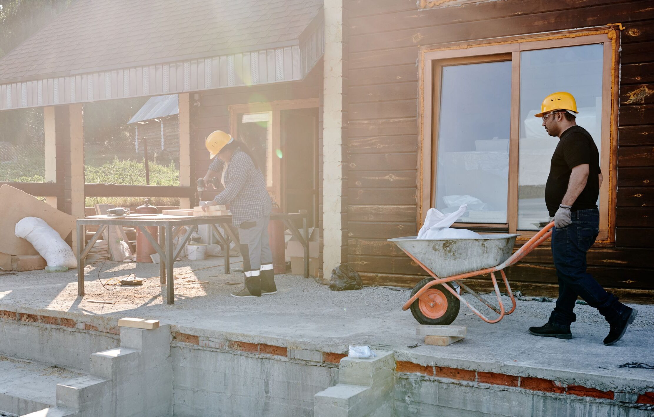 Two construction workers renovating a house exterior, carrying materials and working on woodwork.